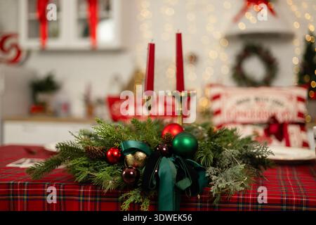 A beautifully decorated Christmas table features red and green ornaments, lush greenery, and elegant candles, setting a festive and cozy atmosphere fo Stock Photo