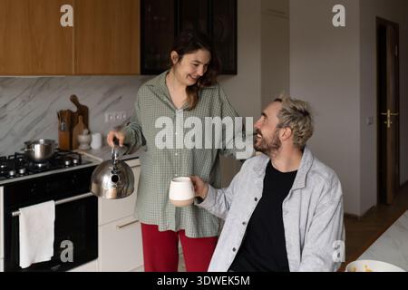 A joyful morning scene of a couple enjoying breakfast together in a cozy kitchen. The woman is pouring coffee while the man holds a mug, surrounded by Stock Photo