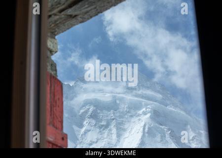 Captivating view of Dent d'Herens in Switzerland, seen through a wooden window frame. The majestic peak is surrounded by clear blue skies and scattere Stock Photo