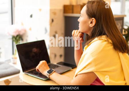 A woman works on her laptop in a stylish cafe, an example of the remote work lifestyle. This informal setting fosters productivity in a relaxed and mo Stock Photo