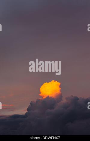 A glowing orange cloud illuminated by the setting sun against a tranquil purple evening sky, capturing the serene beauty and contrast of nature's colo Stock Photo