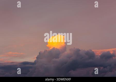 A beautiful view of towering clouds tinged with vibrant orange sunlight, contrasting against a soft purple sky during sunset, creating a serene and ma Stock Photo