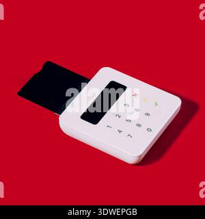 A modern white card reader with a black screen and buttons is placed on a vibrant red background, symbolizing festive Christmas shopping and holiday p Stock Photo