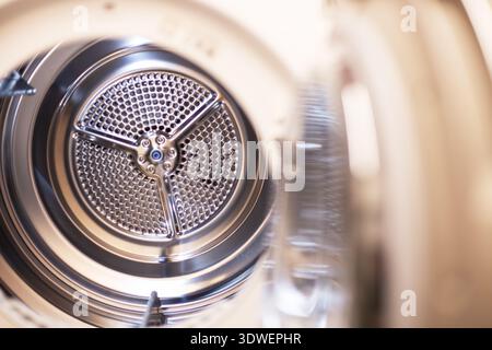 Dryer interior showing clean perforated stainless steel drum ready for clothes. Clean metallic drum inside washing machine for laundry tasks. Stock Photo