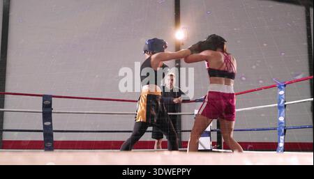 Jabbing boxer in black top gold-trim shorts extending arm in gym ring, with gloves and headgear Stock Photo