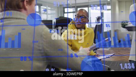 Holding man in yellow pullover and glasses presenting document in modern office, with blue charts Stock Photo