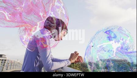 Leaning woman in dark headscarf purple sport top on bridge railing, jellyfish holograms, copy space Stock Photo