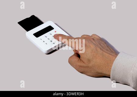 Hand enters pin on a compact card reader, illustrating a cashless transaction process. Highlights ease of digital payments in modern financial systems Stock Photo