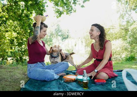 Two sisters share laughter and joy during a relaxing picnic in the park. Seated on a blanket, they enjoy the sunny day, food, and the playful company Stock Photo