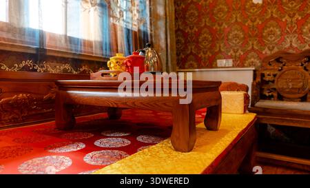 A traditional Chinese tea set with red and yellow teapots on a wooden table, adorned with intricate carving, located in a richly decorated room in Pin Stock Photo