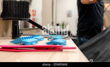 A variety of barbershop tools, including clippers, combs, and brushes, are neatly arranged on a wooden counter. The background features a barber prepa Stock Photo