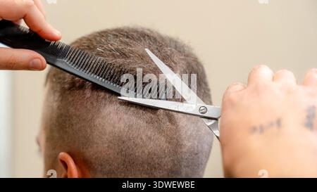 A barber skillfully trims a client's hair using scissors and comb in a barbershop. The close-up image highlights the precision and technique involved Stock Photo