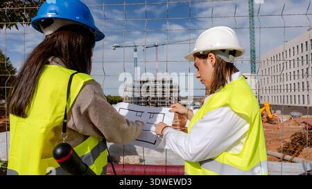 Female architect and technical engineer consult construction plans on site. Wearing safety gear, they assess progress and collaborate on building proj Stock Photo