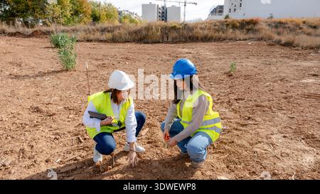 An architect and a technical engineer are inspecting a construction site. Both are wearing safety helmets and high visibility vests, collaborating on Stock Photo