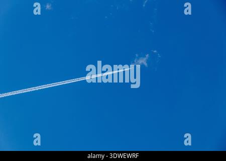 A high-flying airplane leaves a long contrail as it soars across a vast, clear blue sky. The image captures the sense of speed, freedom, and vastness Stock Photo