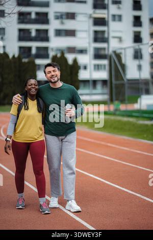Diverse couple smiling on running track, enjoying fitness together Stock Photo