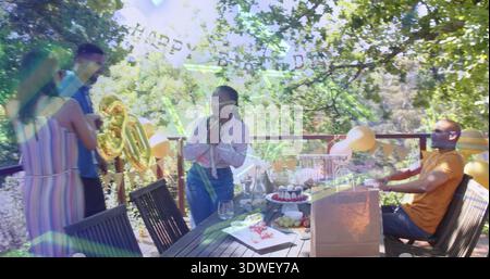 Holding microphone, woman in pink blouse speaking on wood deck, with gold 30 balloons and cupcakes Stock Photo