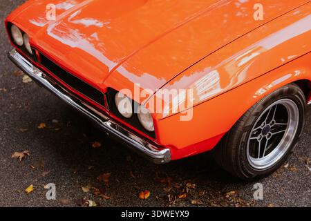 Close-up of a vintage orange car showing its shiny chrome details and classic design, parked on a leaf-covered street, capturing a nostalgic automotiv Stock Photo