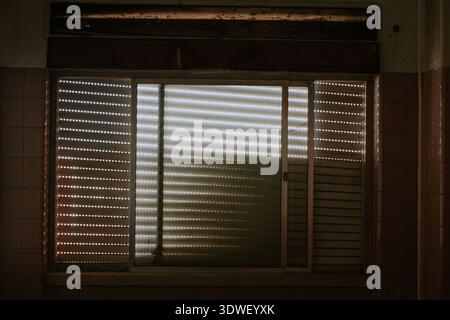 Soft light filters through the slatted window blinds of a dim room, creating a calming pattern of shadows and highlights. The subdued atmosphere sugge Stock Photo