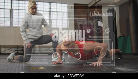 Performing man holding push-up in red top in gym on rubber floor, trainer kneeling coaching HUD Stock Photo