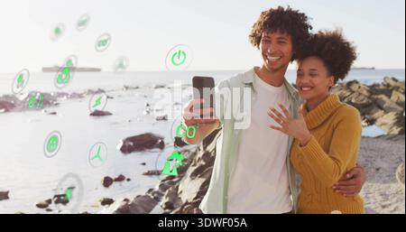 Smiling couple taking phone selfie on rocky shore showing ring yellow sweater AR icons, copy space Stock Photo