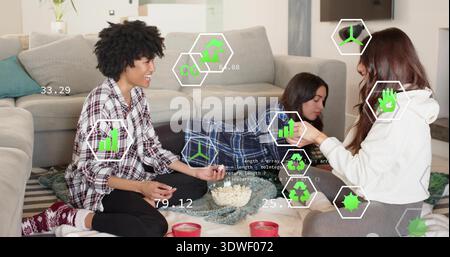 Chatting three women in loungewear lounging on rug at home, popcorn bowl, red mugs, green overlays Stock Photo