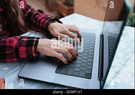 A person types on a laptop while wearing a red plaid shirt, capturing the essence of a calm morning routine. The scene unfolds on a table, set in a re Stock Photo
