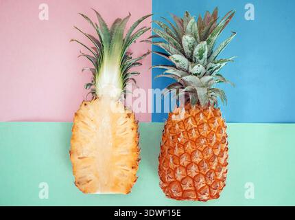 A fresh, ripe pineapple split in half, showcasing its juicy interior on a vibrant pink and blue background. The tropical fruit’s spiky leaves add an e Stock Photo