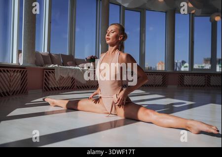 A beautiful woman practicing yoga in a bright studio, doing the splits with large windows casting deep, beautiful shadows across the floor. Stock Photo