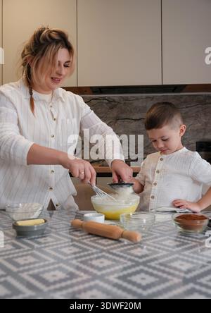 A mother and child enjoy bonding time baking in their kitchen. The scene captures the joy and warmth of parenting, emphasizing love, support, and fami Stock Photo