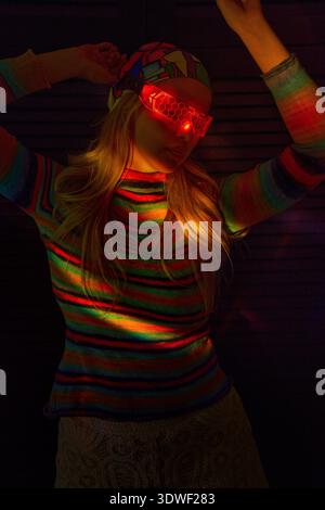 A blonde woman explores virtual reality, wearing a VR set and a colorful headscarf. The atmospheric lighting creates a striking and futuristic mood, h Stock Photo