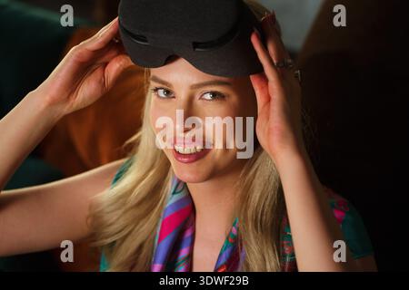 A blond woman with a cheerful expression uses a virtual reality gadget. She is immersed in a digital experience, showcasing the excitement and potenti Stock Photo
