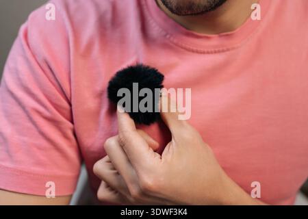 Close-up cropped shot of content creator preparing for recording session by placing small, modern wireless lavalier microphone onto pink shirt using Stock Photo
