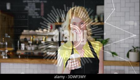 Standing barista holding to-go cup wearing black apron yellow top at cafe with espresso machine HUD Stock Photo