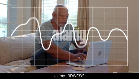 Leaning senior man in blue tee using laptop, holding smartphone at home living room, grid overlay Stock Photo