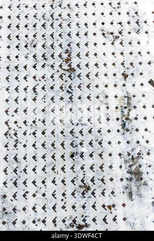 Abstract background of a diamond plate metal surface partially covered with white snow. Industrial texture showing non-slip safety pattern in winter c Stock Photo