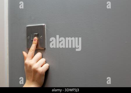 Close-up of a person toggling a wall-mounted light switch, switching the light on or off. Concept image representing electricity use, energy control Stock Photo