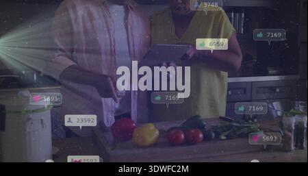 Using tablet senior couple chopping peppers on board in kitchen woman wearing yellow social bubbles Stock Photo