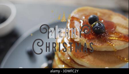 Showing pancake stack shining on tabletop with blueberries, maple syrup, Merry Christmas overlay Stock Photo