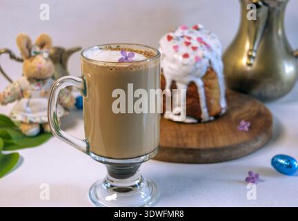 Action shot of milk being poured from a creamer into a coffee cup. Traditional Easter cake, lilac flowers, and a plush bunny in a skirt on a breakfast Stock Photo
