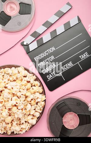 Movie clapper with popcorn and film reels on pink background. Vertical photo Stock Photo