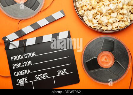 Movie clapper with popcorn and film reels on orange background. Top view Stock Photo