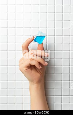 Close-up of a hand holding a blue laundry capsule in front of a white tiled wall. The image highlights the convenience and compact design of the laund Stock Photo