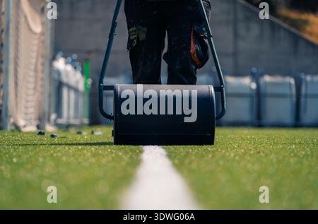 A close-up view of a worker using a field roller to repaint white lines on a soccer field, highlighting the process of field renovation and maintenanc Stock Photo