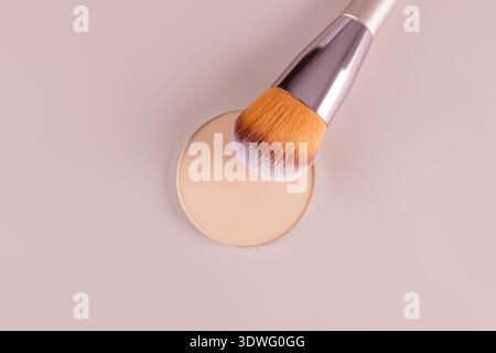 A close-up of a cosmetic face powder compact accompanied by a makeup brush on a soft pink background. Perfect for illustrating beauty, skincare, and c Stock Photo
