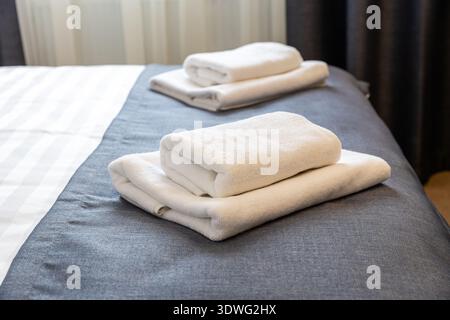 Folded white towels on hotel bed close up with clean modern hospitality interior Stock Photo
