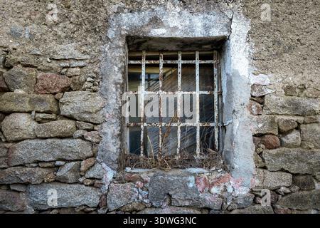 Close-up detail of an ancient window with a rusted wrought iron grating on a stone house in the medieval village of Lollove. The image captures the es Stock Photo
