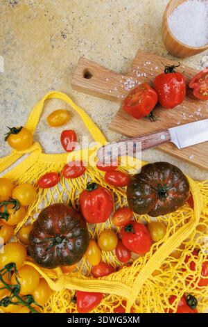 Organic tomatoes in yellow mesh bag and knife on kitchen board Stock Photo