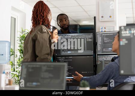 Multiethnic individuals analyzing code on multiple monitors, planning on improving frontend interface for clients. Professional team of developers working on web development project. Stock Photo