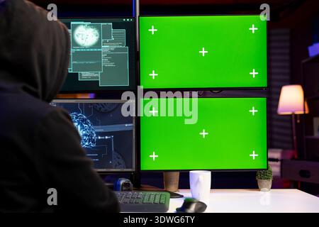 Hooded hacker installing spyware using isolated screen PC and AI to secretly gather data about victims. Rogue technician coding exploits using mockup multi monitor setup to gain unauthorized access Stock Photo
